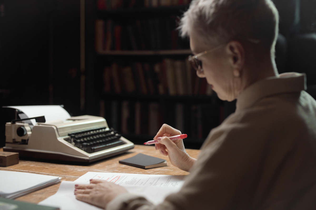 Person reviewing documents in a library with a vintage typewriter, embodying focused research or study.